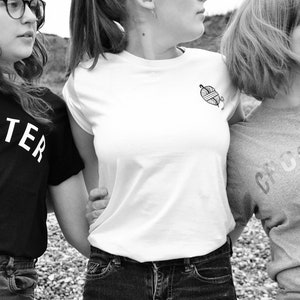 Puede incluir: Tres amigas con camisetas negras, blancas y grises con las palabras "Knitter", "Crocheter" y un gr&aacute;fico de ovillo de lana.