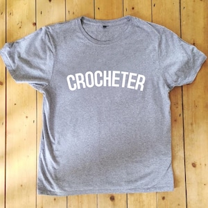 May include: A grey t-shirt with the word "CROCHETER" printed in white on the front.