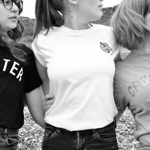 Puede incluir: Tres amigas con camisetas negras, blancas y grises con las palabras "Knitter", "Crocheter" y un gr&aacute;fico de ovillo de lana.
