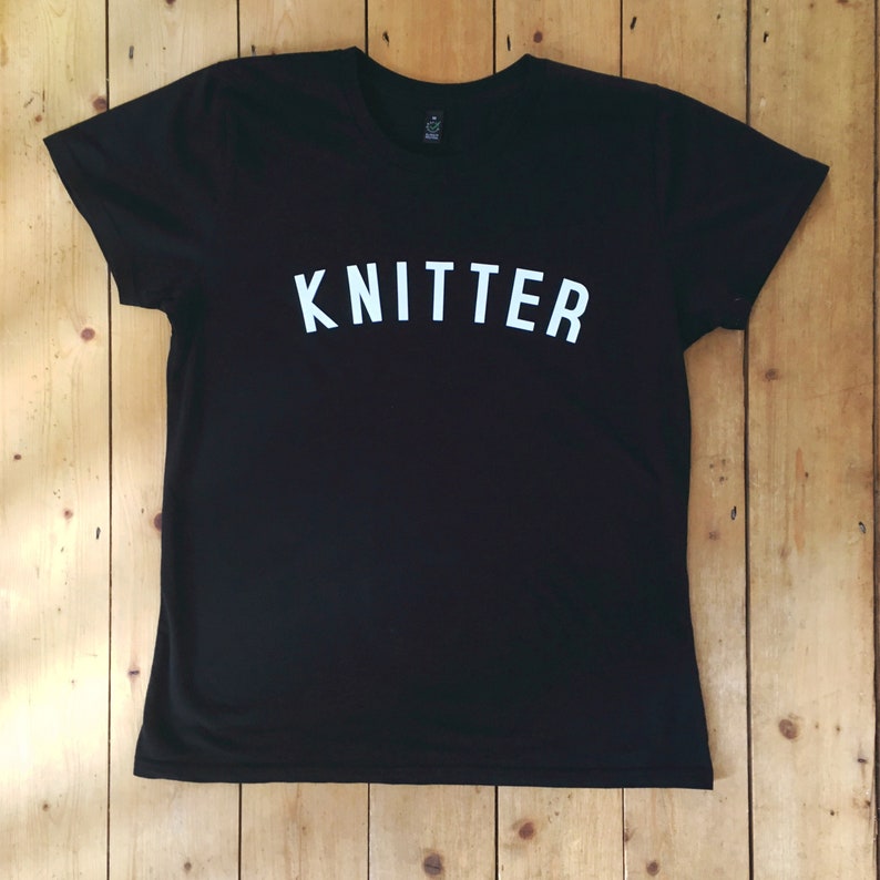 Puede incluir: Camiseta negra con la palabra "KNITTER" impresa en blanco en la parte delantera.