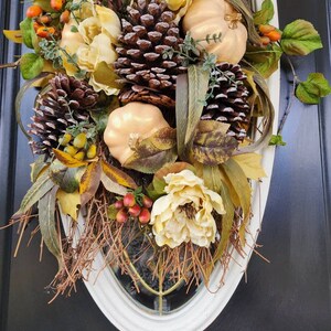 Op de afbeelding: Een herfst-deurkrans met nep-pompoenen, dennenappels en bloemen in tinten van bruin, goud en cr&egrave;me.