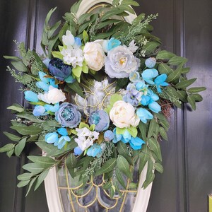 May include: A blue and white floral wreath with green leaves, hanging on a black door.