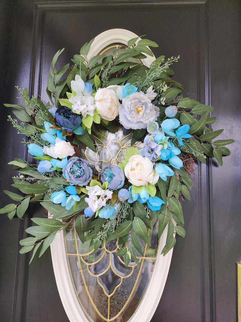 May include: A blue and white floral wreath with green leaves, hanging on a black door.