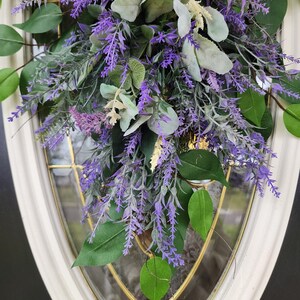 Peut inclure: Gros plan sur une composition florale avec des brins de lavande violets, des feuilles vertes et un feuillage gris-vert. L'arrangement est plac&eacute; devant une porte vitr&eacute;e &agrave; cadre blanc. La lavande et la verdure cr&eacute;ent un affichage naturel et accueillant.