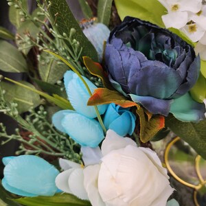 May include: A wreath featuring blue, white and green flowers. The wreath is made from artificial flowers and greenery.