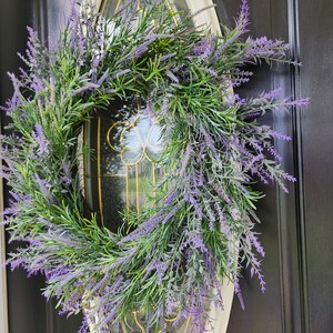 May include: A purple and green lavender wreath with a white oval frame. The wreath is hanging on a black door.