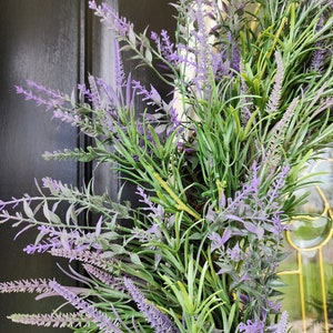 May include: A lavender wreath with purple and green foliage. The wreath is made of artificial flowers and is perfect for adding a touch of spring to your home decor.