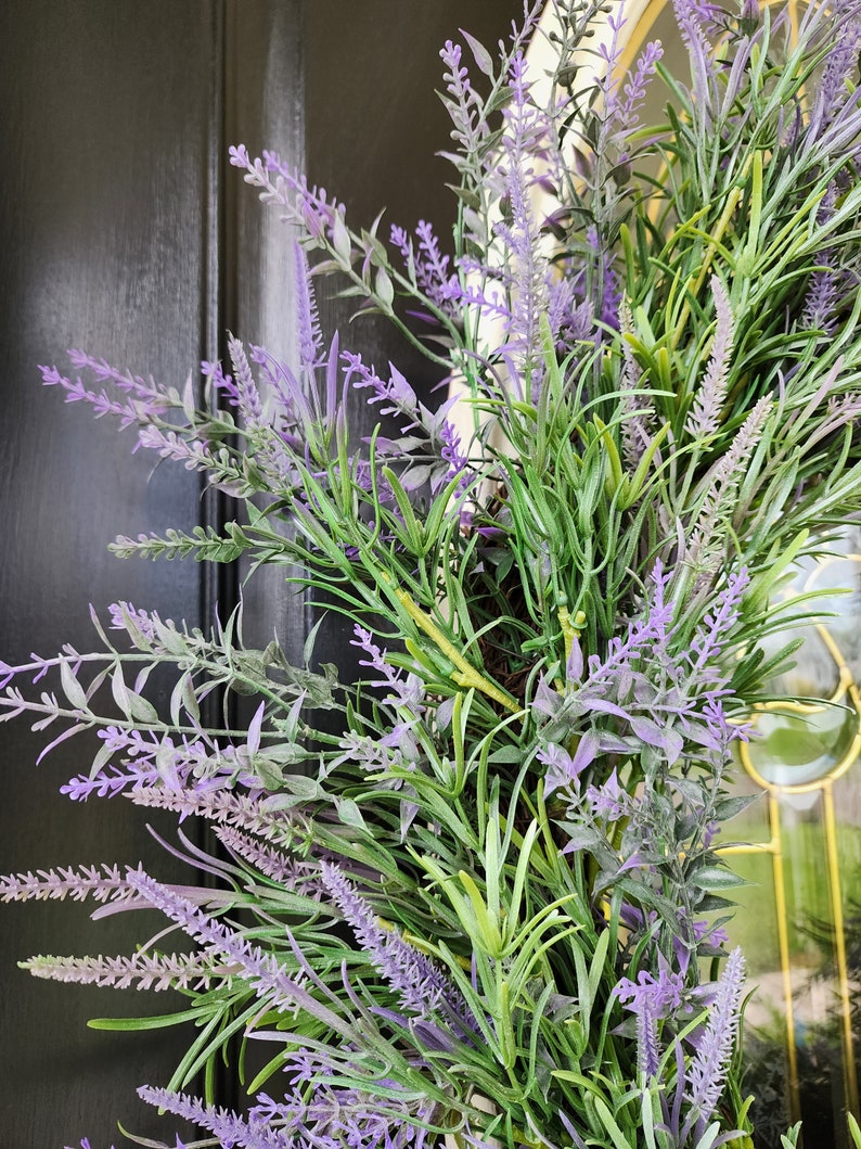 May include: A lavender wreath with purple and green foliage. The wreath is made of artificial flowers and is perfect for adding a touch of spring to your home decor.