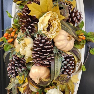 Op de afbeelding: Een herfstkrans met gouden pompoenen, dennenappels en kunstbloemen in cr&egrave;me- en bruintinten. De krans is versierd met herfstbladeren en bessen.