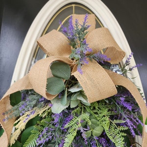 Peut inclure: Une couronne d&eacute;corative avec un n&oelig;ud en toile de jute et un arrangement de lavande artificielle, de feuillage vert et de feuilles d'eucalyptus. La couronne est con&ccedil;ue pour &ecirc;tre accroch&eacute;e &agrave; une porte ou &agrave; un mur, ajoutant une touche de beaut&eacute; naturelle.