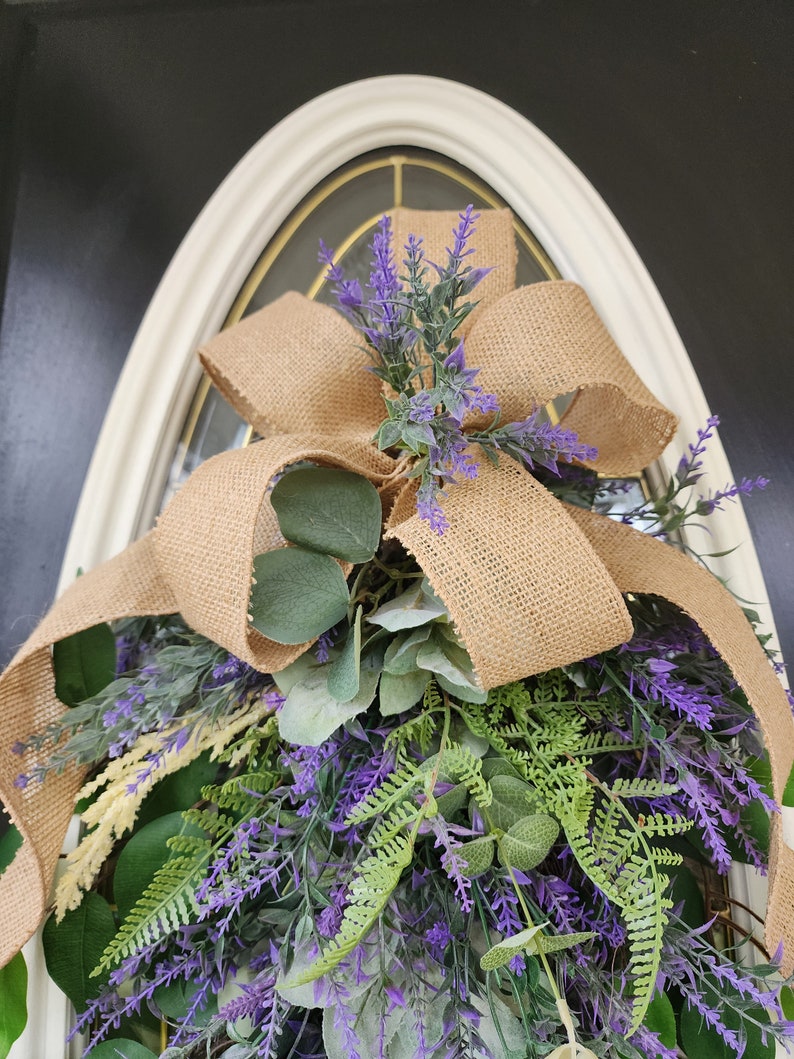 Peut inclure: Une couronne d&eacute;corative avec un n&oelig;ud en toile de jute et un arrangement de lavande artificielle, de feuillage vert et de feuilles d'eucalyptus. La couronne est con&ccedil;ue pour &ecirc;tre accroch&eacute;e &agrave; une porte ou &agrave; un mur, ajoutant une touche de beaut&eacute; naturelle.