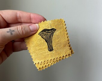 May include: A stack of small, yellow fabric squares with a black and white illustration of a mushroom printed on each square.