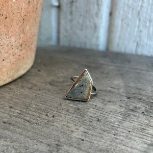 May include: A silver ring with a gray and brown ceramic stone in a triangular shape.