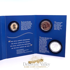 May include: A blue presentation folder containing three coins: a gold-colored Ronald Reagan dollar, a bronze medal featuring Ronald and Nancy Reagan, and a silver American Eagle coin. The folder includes printed text detailing the coin specifications.