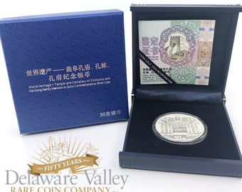 May include: A silver coin in a blue box with a black interior. The coin features a depiction of a building with the text "10元" and "孔林、孔府" in Chinese characters. The box has the text "世界遗产————曲阜孔庙、孔林、孔府纪念银币" in Chinese characters and "World Heritage-Temple and Cemetery of Confucius and the Kong Familly Mansion in Qulu Commemorative Silver Coin" in English. The box also has the text "30克银币" in Chinese characters.