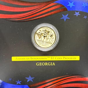 May include: A gold-colored coin with the inscription "GEORGIA TRUSTEES GARDEN UNITED STATES OF AMERICA". The coin is displayed in a black and red frame with stars and the text "AMERICAN INNOVATION™ $1 COIN PROGRAM GEORGIA".