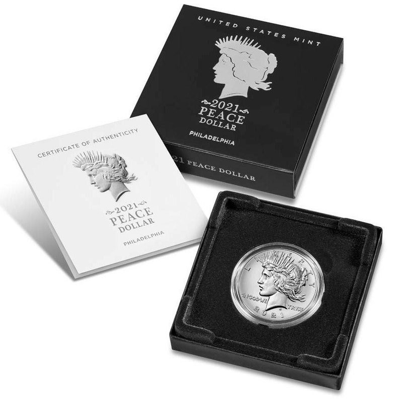 May include: A silver 2021 Peace Dollar coin in a black velvet box with a certificate of authenticity. The coin features a profile of a woman with a crown of olive branches and the inscription "2021 Peace Dollar" on the obverse.