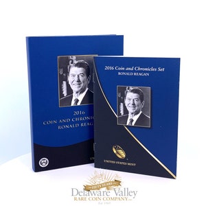 May include: A 2016 Coin and Chronicles Set featuring Ronald Reagan, consisting of a blue and black presentation folder and a matching slipcase. Both items display a black and white portrait of Ronald Reagan and the text 2016 Coin and Chronicles Set Ronald Reagan, with the United States Mint logo.