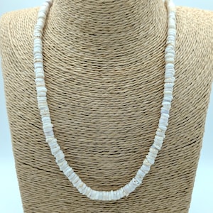 May include: A white shell necklace displayed on a tan bust. The necklace is made of small, flat, irregular shell pieces strung together. The shells have a natural, off-white color with subtle variations.