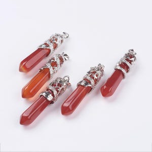 May include: Six red-orange gemstone pendants with silver-colored dragon-themed caps. The pendants are hexagonal in shape and vary slightly in color. The caps have a detailed dragon design and a loop for hanging.