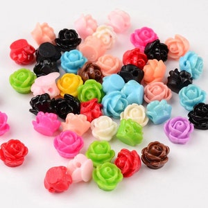 Könnte beinhalten: Sortiment an bunten Kunststoffrosenperlen. Die Perlen sind in verschiedenen Farben, darunter rosa, rot, blau, grün, gelb und schwarz. Die Perlen sind klein und haben eine 3D-Rosenform.