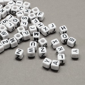 Könnte beinhalten: Weiße Kunststoffbuchstabenperlen mit schwarzer Beschriftung. Die Buchstaben umfassen A, B, C, D, F, G, H, I, J, L, M, N, O, P, Q, S, W, X, Y und Z.
