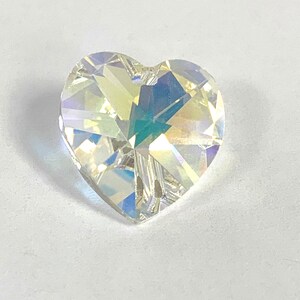 May include: A clear iridescent heart-shaped crystal with a faceted design. The crystal has a hole at the top for hanging.