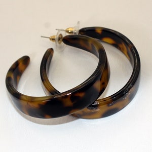 Può includere: Un paio di orecchini a cerchio in tartaruga marrone e nero. Gli orecchini sono realizzati in plastica spessa e resistente e hanno una finitura liscia e lucida.