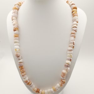 Op de afbeelding: Een lange ketting gemaakt van witte en bruine schelp kralen. De ketting wordt getoond op een wit mannequin.