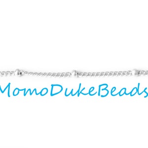 Op de afbeelding: Zilveren ketting met kleine ronde kralen, een gedraaid kettingontwerp en de tekst "MomoDukeBeads".