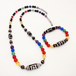 May include: A black and white beaded necklace and bracelet set with colorful beads. The necklace and bracelet feature a black and white patterned bead with a silver accent. The colors of the beads are red, orange, yellow, green, blue, and purple.