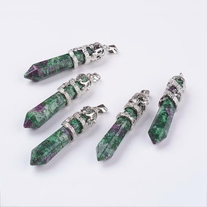 May include: Five gemstone pendants with a green and purple speckled pattern. Each pendant has a silver-colored metal cap with a decorative design and a loop for a chain. The pendants are displayed on a white surface.