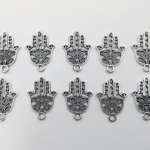 Könnte beinhalten: Zehn silberfarbene Metall-Anhänger in Form einer Hamsa-Hand mit filigranen Details. Die Anhänger haben eine Öse oben zum Anbringen an Schmuck oder andere Bastelarbeiten.