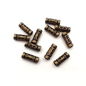 Peut inclure: Un groupe de 12 perles en métal de couleur or antique avec un motif orné. Les perles sont de forme cylindrique et ont une finition lisse et polie.