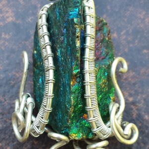 May include: A silver wire wrapped pendant featuring a green, iridescent, and gold gemstone. The pendant has a unique, organic design with multiple loops and swirls.