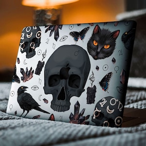 Może przedstawiać: Laptop z czarno-białym wzorem przedstawiającym czaszkę, czarnego kota, kruka, kryształy i symbole astrologiczne. Wz&oacute;r znajduje się na białym tle.