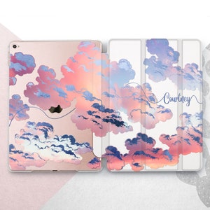 Könnte beinhalten: Eine weiße iPad-Hülle mit einem rosafarbenen und blauen Aquarell-Wolkenmuster. Die Hülle hat eine Klappe, die über den Bildschirm klappt, und einen personalisierten Namen, "Courtney", der auf der Rückseite in Kursivschrift geschrieben ist.