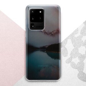 Pu&ograve; includere: Una custodia per telefono trasparente con un'immagine di paesaggio di un lago e montagne. La custodia ha il logo Samsung in basso e il testo "5G100X" sul retro.