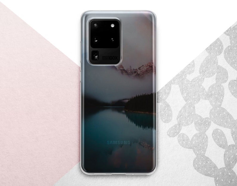 Pu&ograve; includere: Una custodia per telefono trasparente con un'immagine di paesaggio di un lago e montagne. La custodia ha il logo Samsung in basso e il testo "5G100X" sul retro.