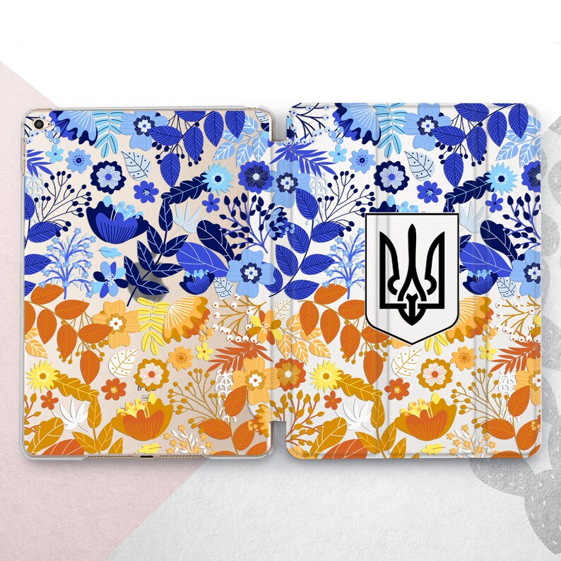 Peut inclure: &Eacute;tui pour tablette &agrave; motifs floraux bleus, oranges et jaunes. L'&eacute;tui a un fond blanc et les armoiries ukrainiennes. Le motif comprend des fleurs et des feuilles.