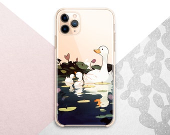 May include: A phone case with a white background and a design of three ducks swimming in a pond with lily pads. The ducks are white with orange beaks and feet. The pond is blue with green lily pads. The phone case is clear and has a gold trim.