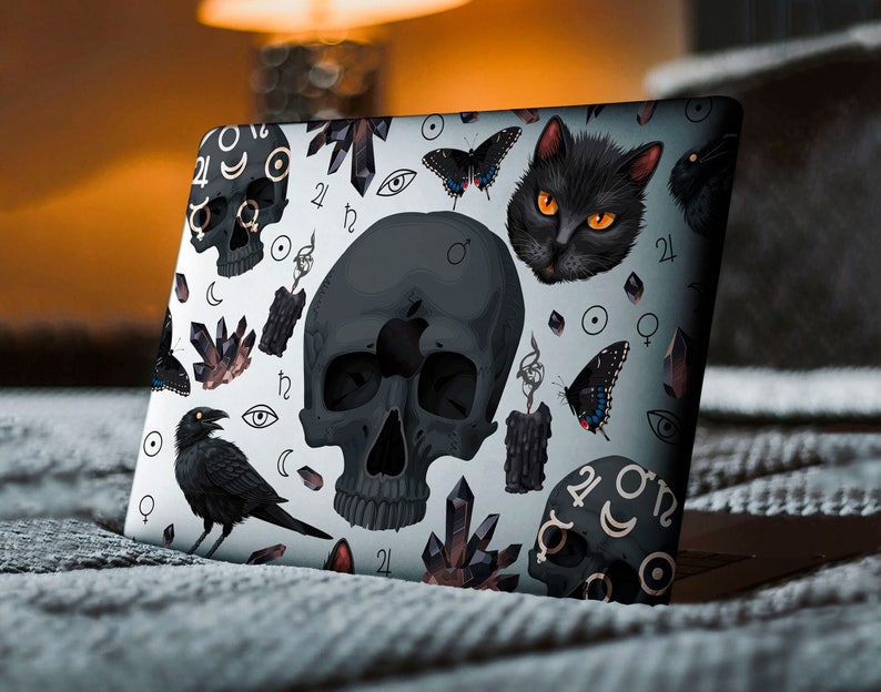 Może przedstawiać: Laptop z czarno-białym wzorem przedstawiającym czaszkę, czarnego kota, kruka, kryształy i symbole astrologiczne. Wz&oacute;r znajduje się na białym tle.