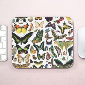 Pode incluir: Um tapete de rato branco com um padrão colorido de borboletas. As borboletas são em vários tons de azul, verde, amarelo, laranja, vermelho e castanho. O tapete de rato é uma ótima maneira de adicionar um toque de natureza à sua secretária.
