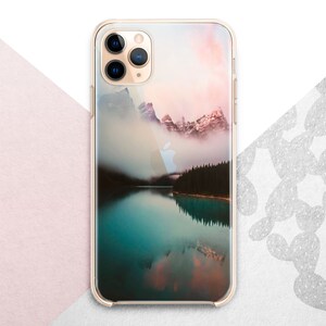 Pu&ograve; includere: Una custodia per telefono trasparente con un'immagine panoramica di un lago di montagna e una foresta nebbiosa. L'immagine ha un cielo di tramonto rosa e arancione.