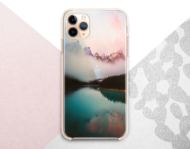 Pu&ograve; includere: Una custodia per telefono trasparente con un'immagine panoramica di un lago di montagna e una foresta nebbiosa. L'immagine ha un cielo di tramonto rosa e arancione.