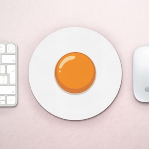 May include: A white round mouse pad with a cartoon image of a fried egg in the center. The egg yolk is orange and the white is white.