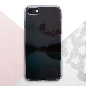 Pu&ograve; includere: Una custodia per telefono trasparente con un'immagine di sfondo nera di un lago di montagna e la parola "iPhone" stampata in basso.