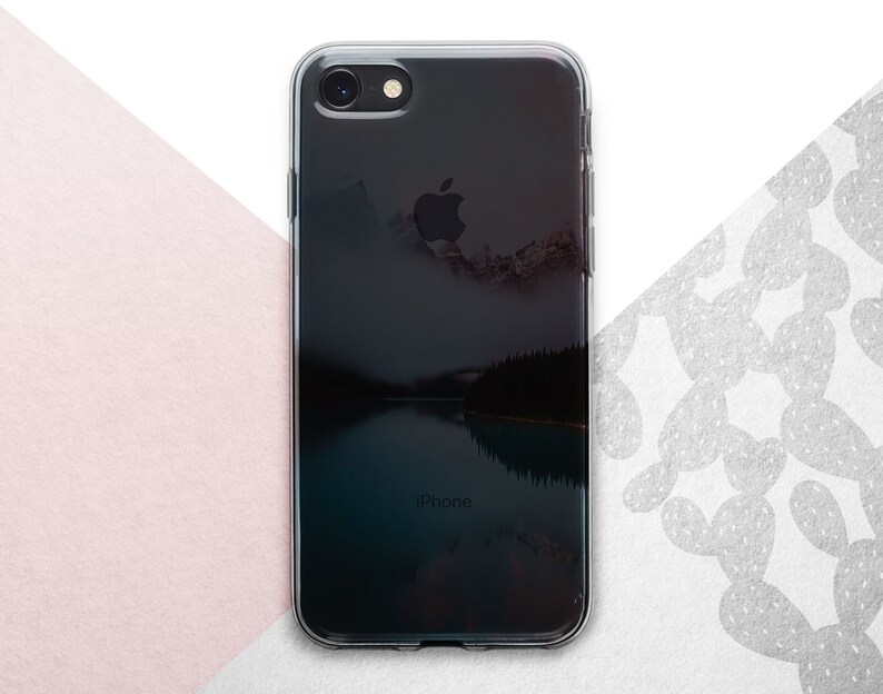 Pu&ograve; includere: Una custodia per telefono trasparente con un'immagine di sfondo nera di un lago di montagna e la parola "iPhone" stampata in basso.