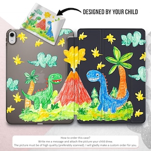 May include: A black iPad case with a colorful drawing of dinosaurs, a volcano, and palm trees. The drawing is designed by a child and says "Designed by your child".