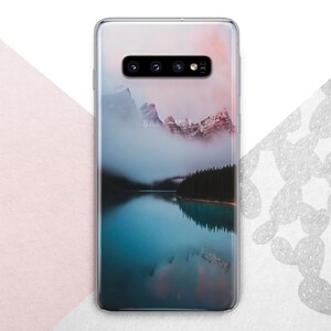 Pu&ograve; includere: Una custodia per telefono trasparente con un'immagine panoramica di una catena montuosa riflessa in un lago. L'immagine &egrave; di un blu e un grigio morbidi e tenui con un tocco di rosa nel cielo.